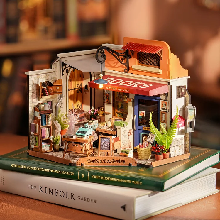 DIY miniature bookstore with nostalgic appearance, colorful exterior, and neatly organized bookcases inside. Outside features rustic wooden table, classic typewriter, potted plants, and baskets.