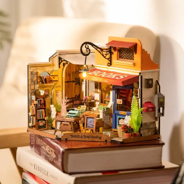 Fully assembled Rolife Corner Bookstore on a stack of books with overhead LED lighting creating a warm ambiance.