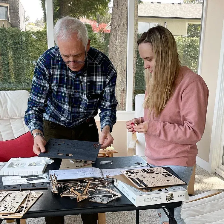 Father and grown daughter assembling a diy 3D puzzle and miniature houses together at a table.