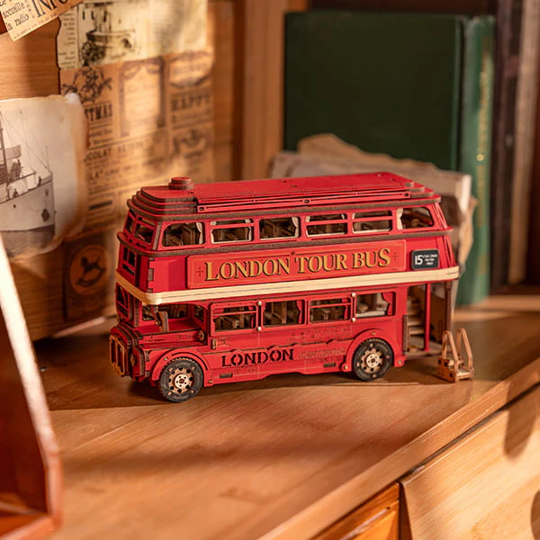 Fully assembled Rolife London Tour Bus 3D Wooden Puzzle kit displayed on a wooden shelf with nostalgic newspaper articles and books in the background.