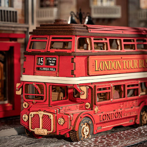 Fully assembled Rolife London Tour Bus 3D Wooden Puzzle kit positioned on a cobbled road next to a city building.