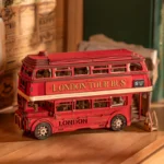 Fully assembled Rolife London Tour Bus 3D Wooden Puzzle kit displayed on a wooden shelf with nostalgic newspaper articles and books in the background.
